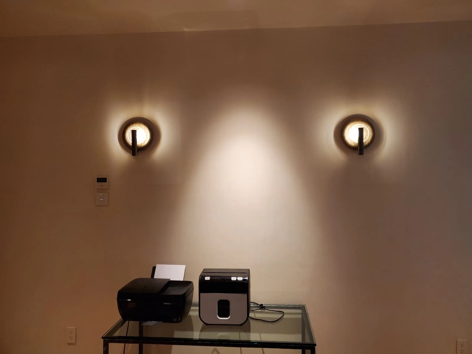 Two illuminated circular wall sconces with controls on the wall below
