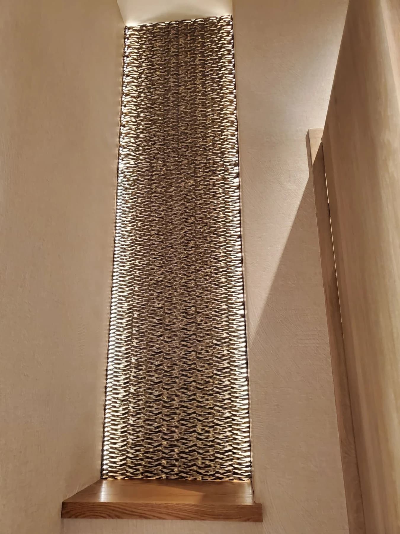 Illuminated textured metal panel in a tall wall alcove