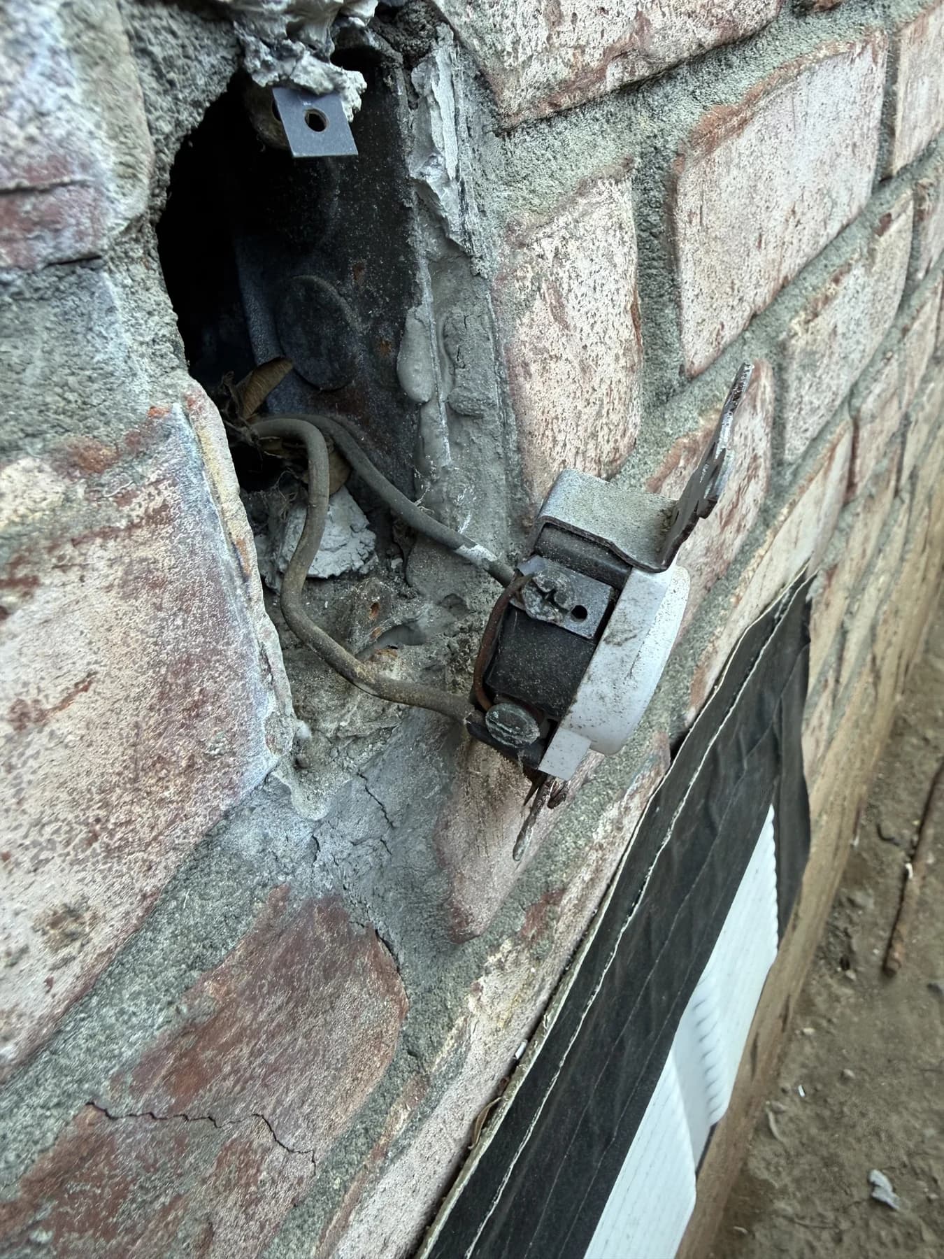 Exterior outlet pulled away from a brick wall with wiring visible