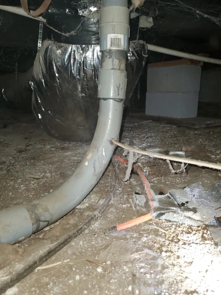 Cable passing through a hole in a pipe beneath a house, beside ductwork and exposed soil