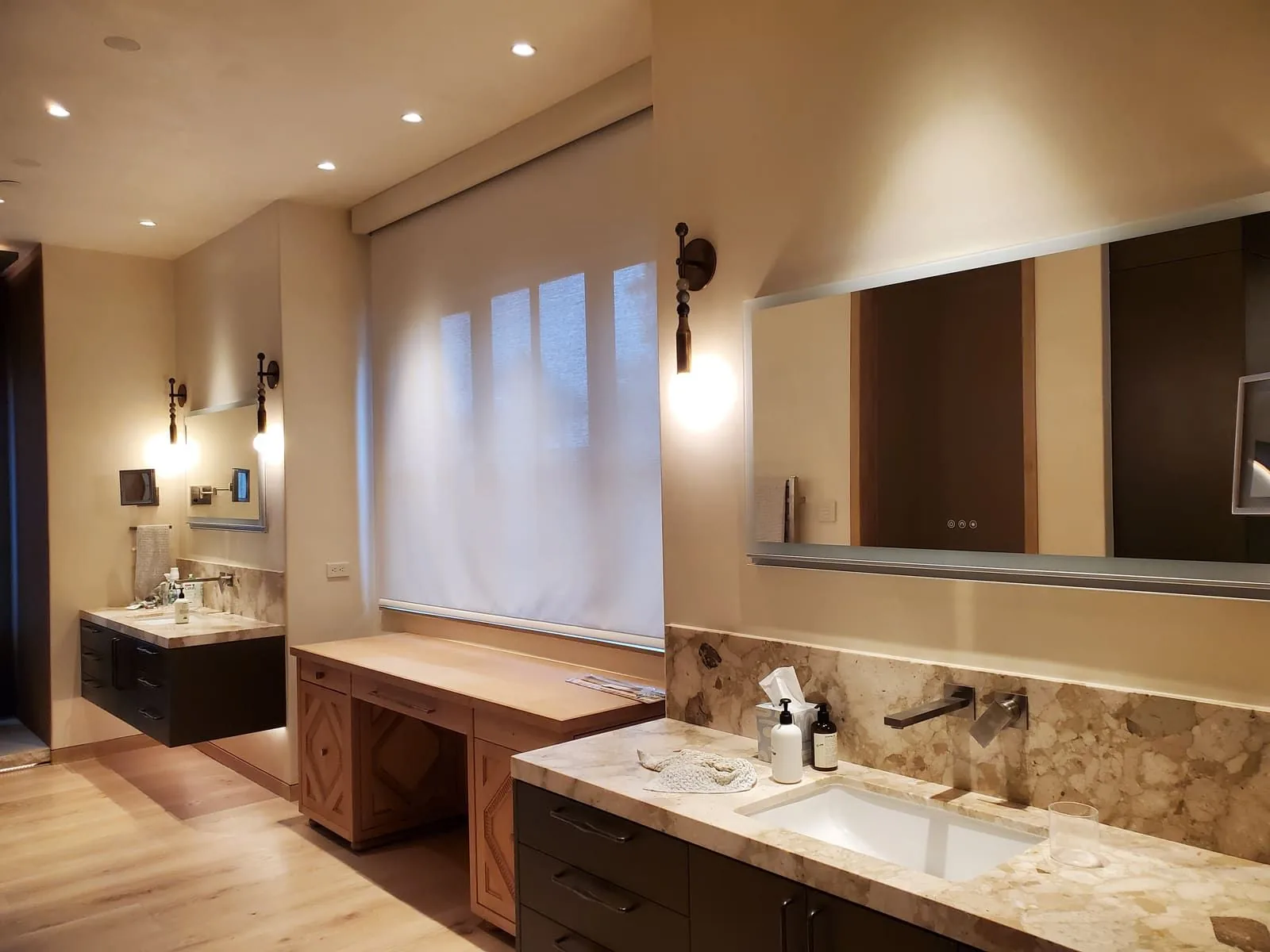 Bathroom vanity with a wide mirror, wall sconces, and recessed ceiling lights